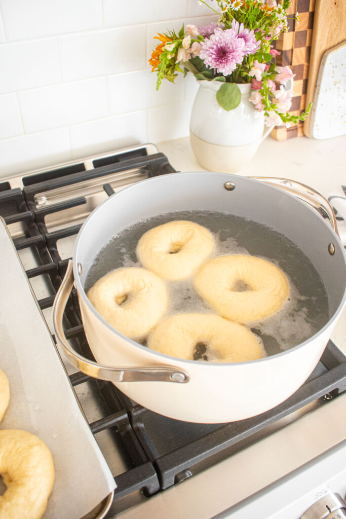 homemade sesame bagels being boiled in a stock pot on a stovetop.