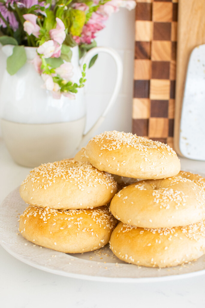 plate of homemade sesame bagels on a white marble counter with a vase of flowers.