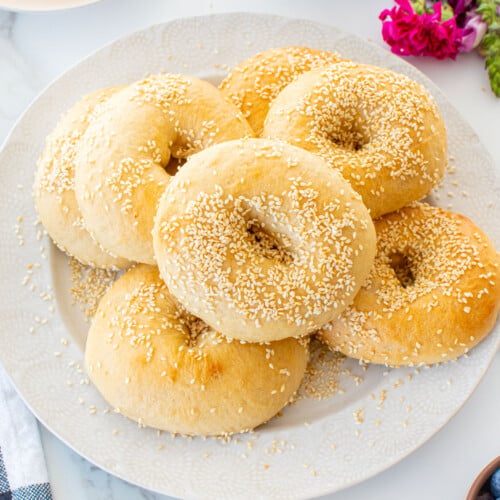 plate of homemade sesame bagels on a white marble table with fruit and juice.