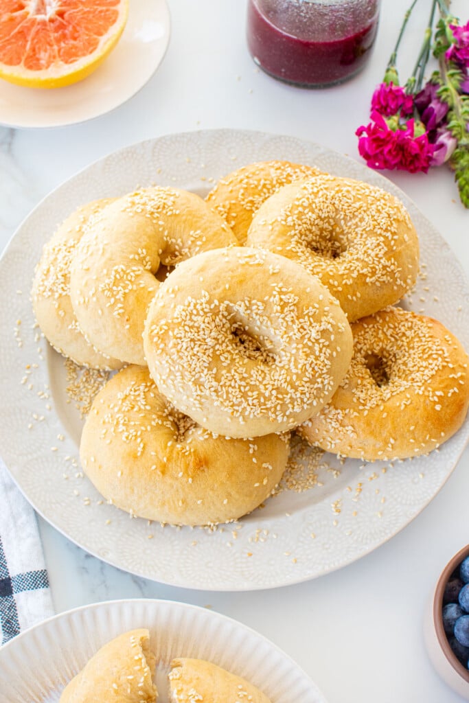 plate of homemade sesame bagels on a white marble table with fruit and juice.