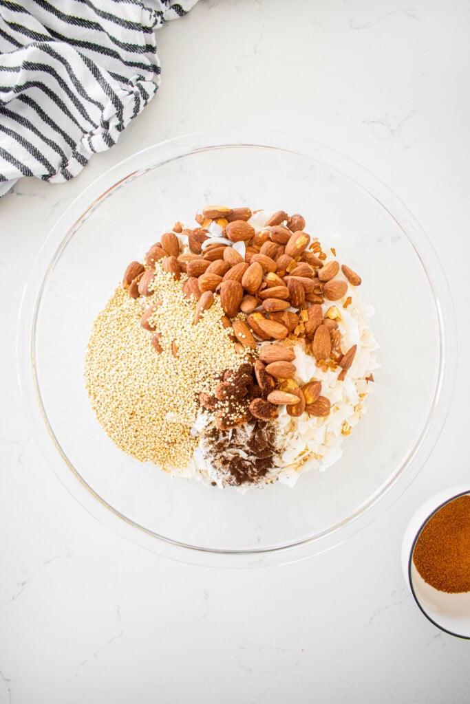 large glass mixing bowl with oats, quinoa, almonds, coconut and vanilla bean on a marble counter.