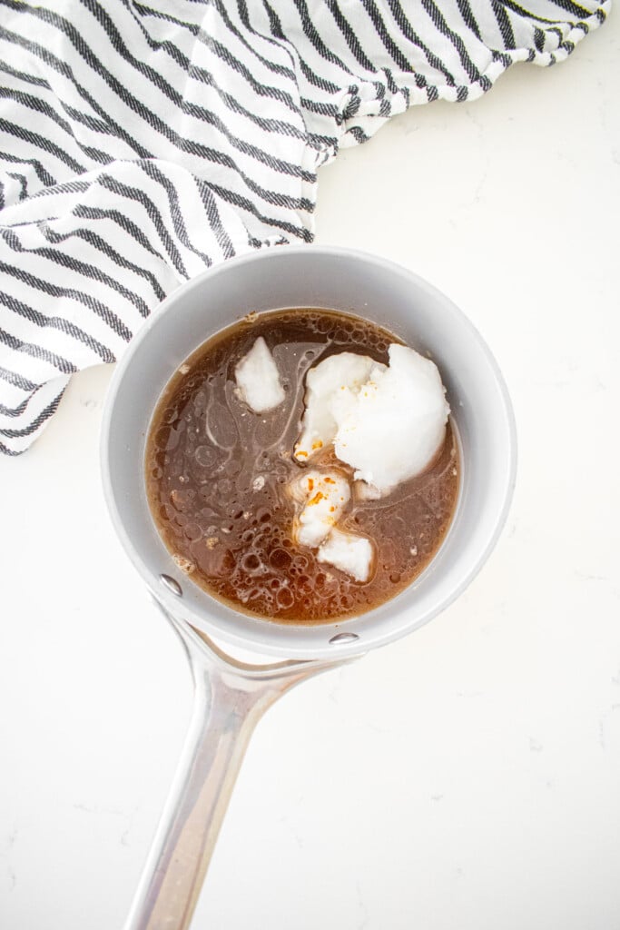 coconut oil, coconut sugar, honey and water in a small pot on a white marble counter.