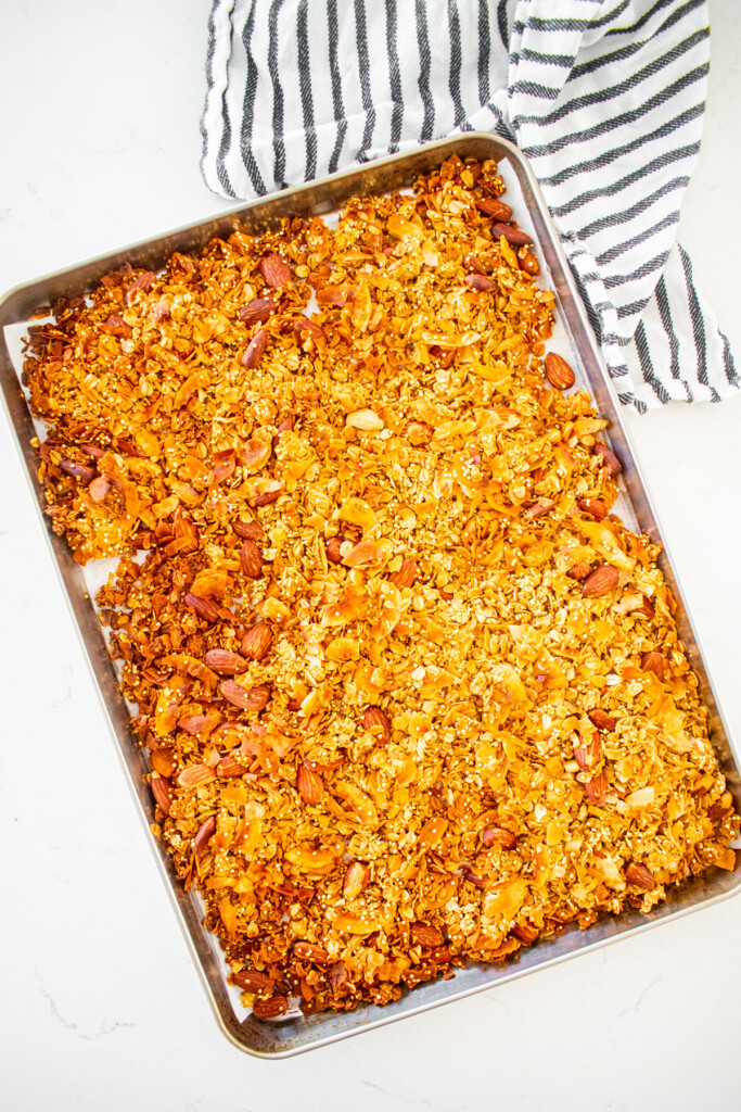 baked honey almond coconut granola on a baking sheet on a white marble counter.