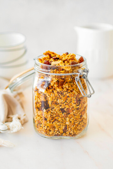 honey almond coconut granola in a glass canister on a marble counter.