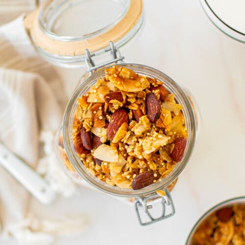 honey almond coconut granola in a glass canister on a marble counter.