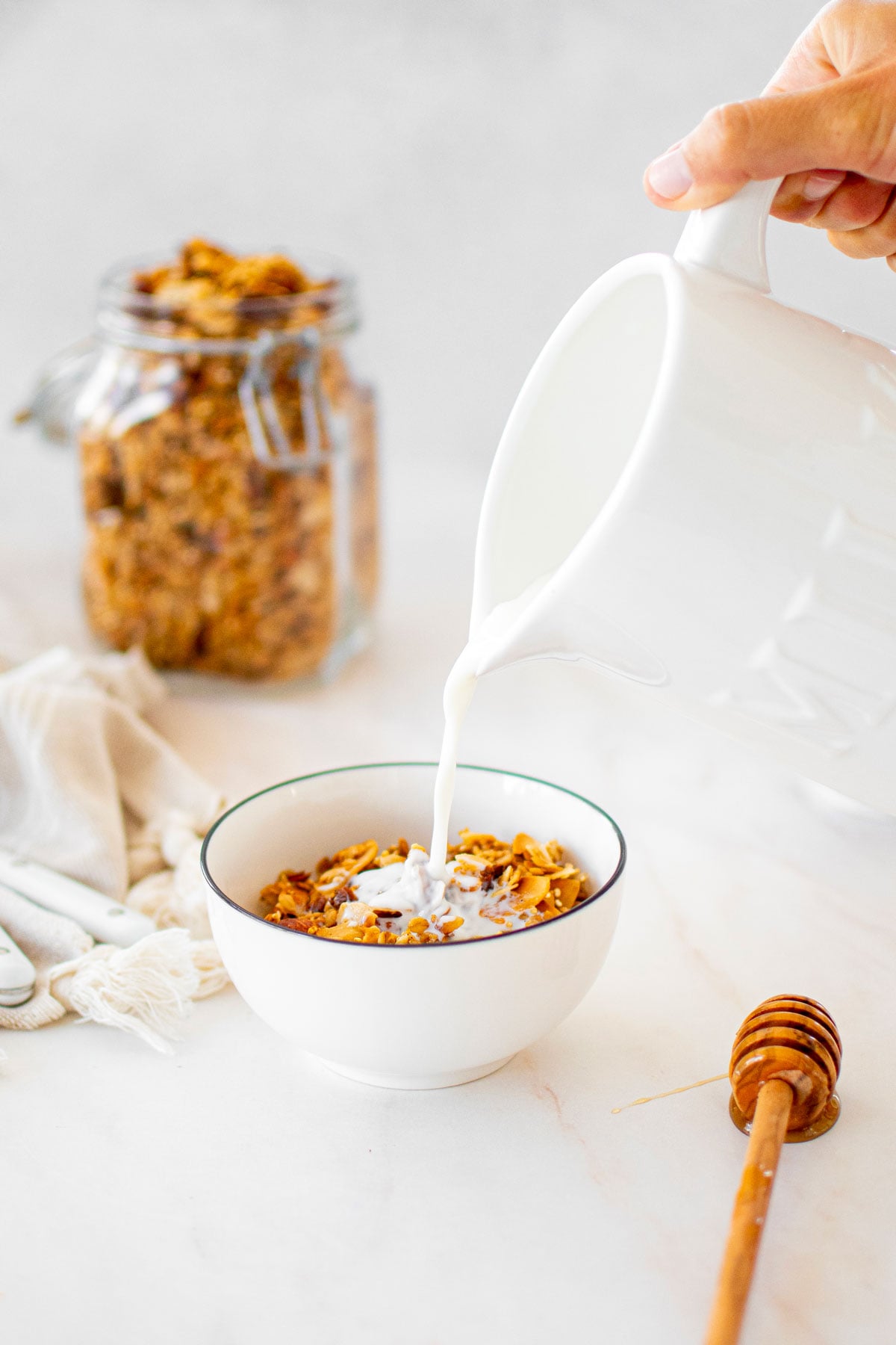 honey almond coconut granola in a bowl with milk being poured into it.