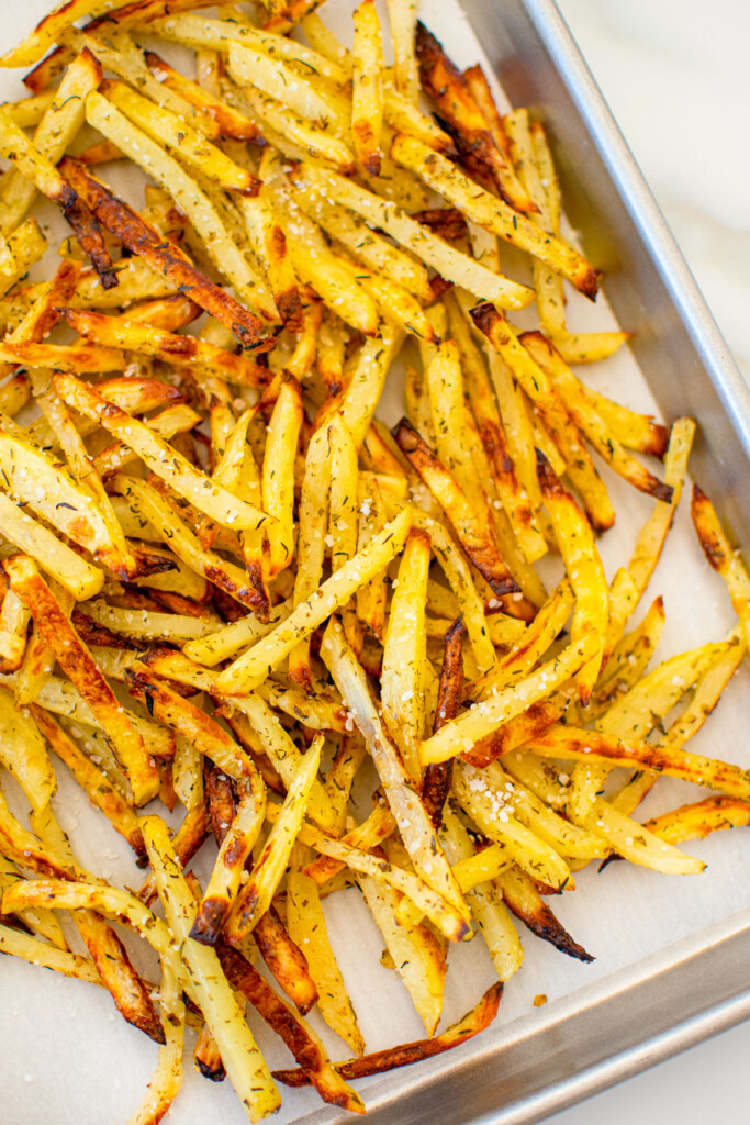 lemon herb french fries on a baking sheet on a white marble countertop.