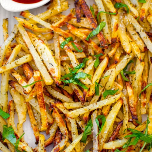 lemon herb french fries with a small dish of ketchup on a baking sheet on a white marble countertop.