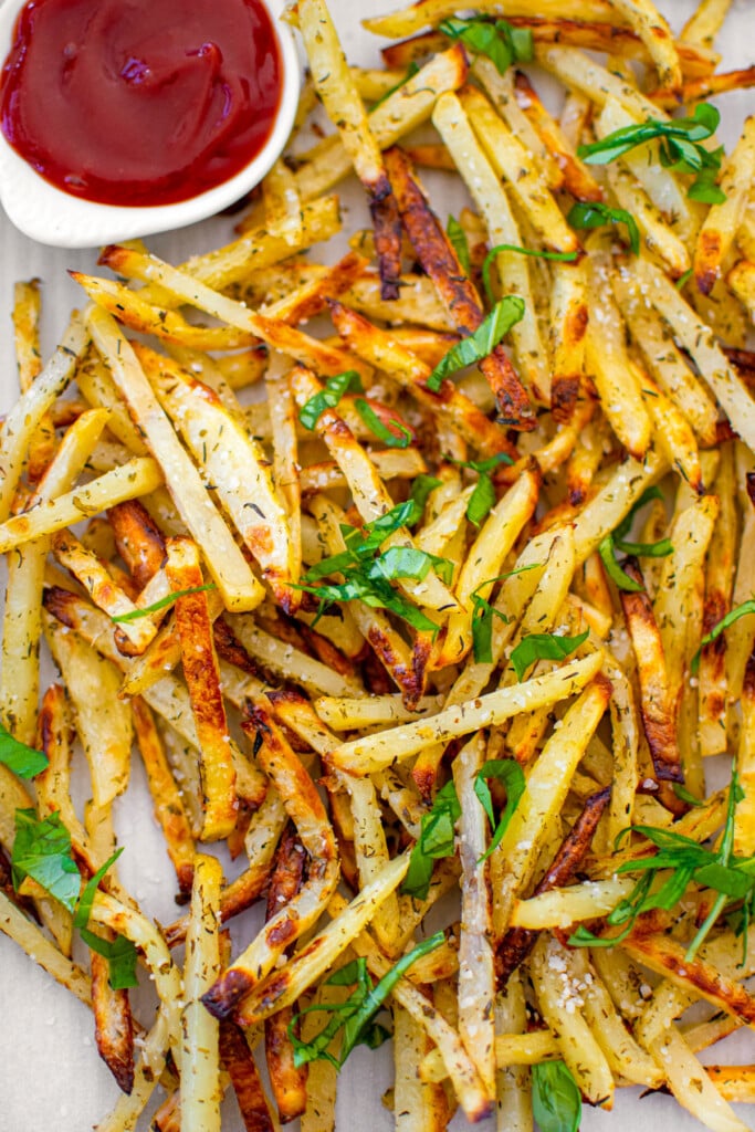 lemon herb french fries with a small dish of ketchup on a baking sheet on a white marble countertop.