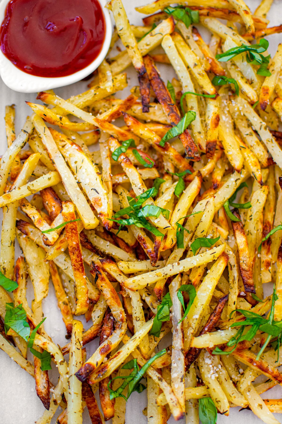lemon herb french fries with a small dish of ketchup on a baking sheet on a white marble countertop.