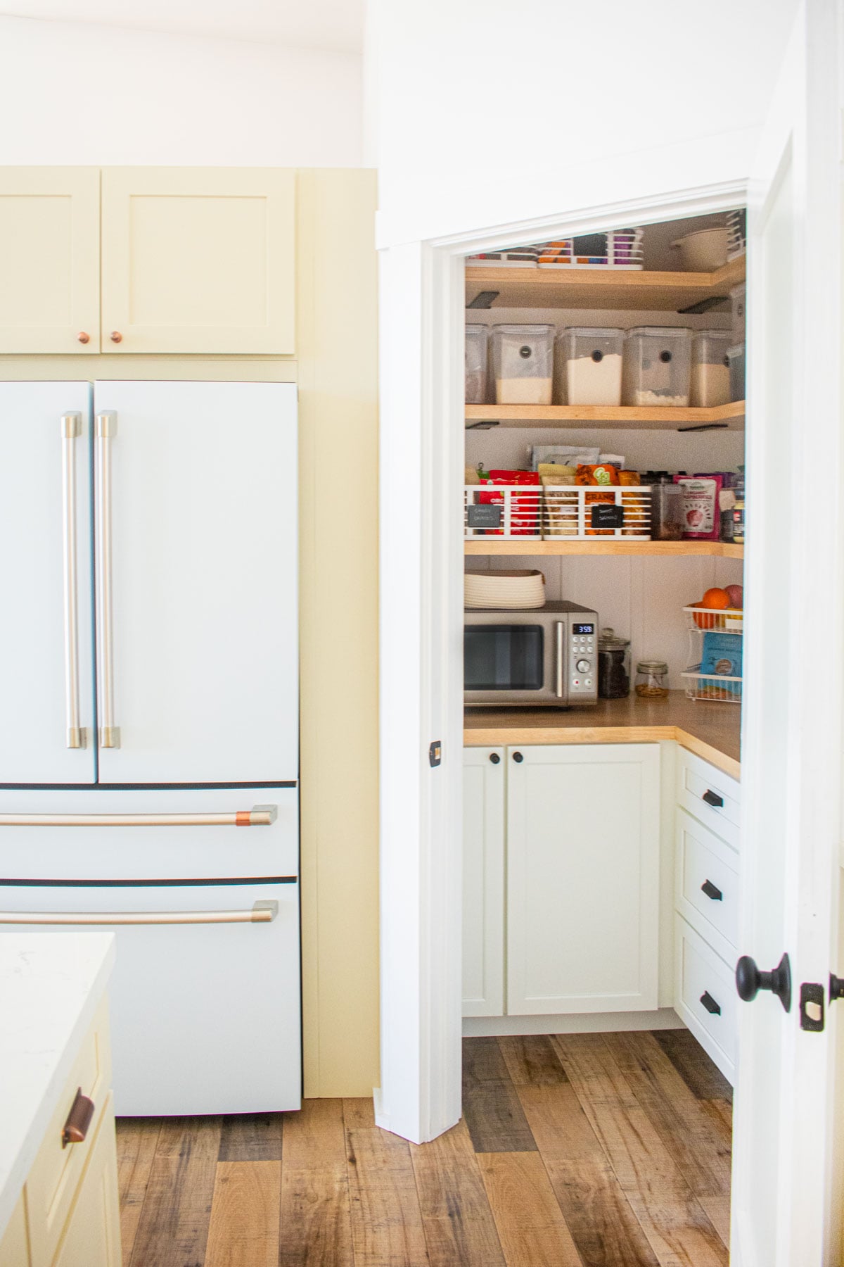 White and tan kitchen with pantry door opening to a diy kitchen corner pantry.