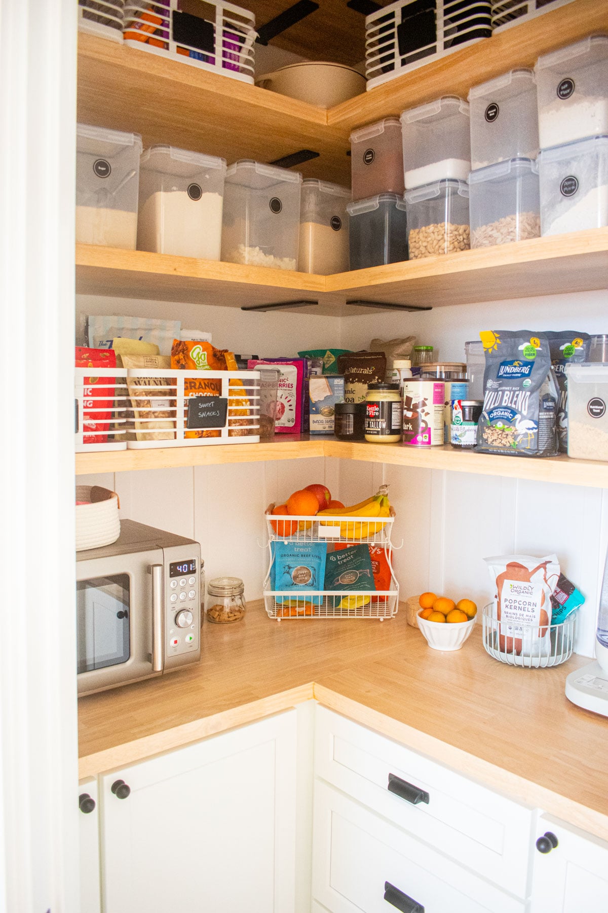 diy kitchen corner pantry with white cabinets and wood counters and wood shelving with pantry storage bins.