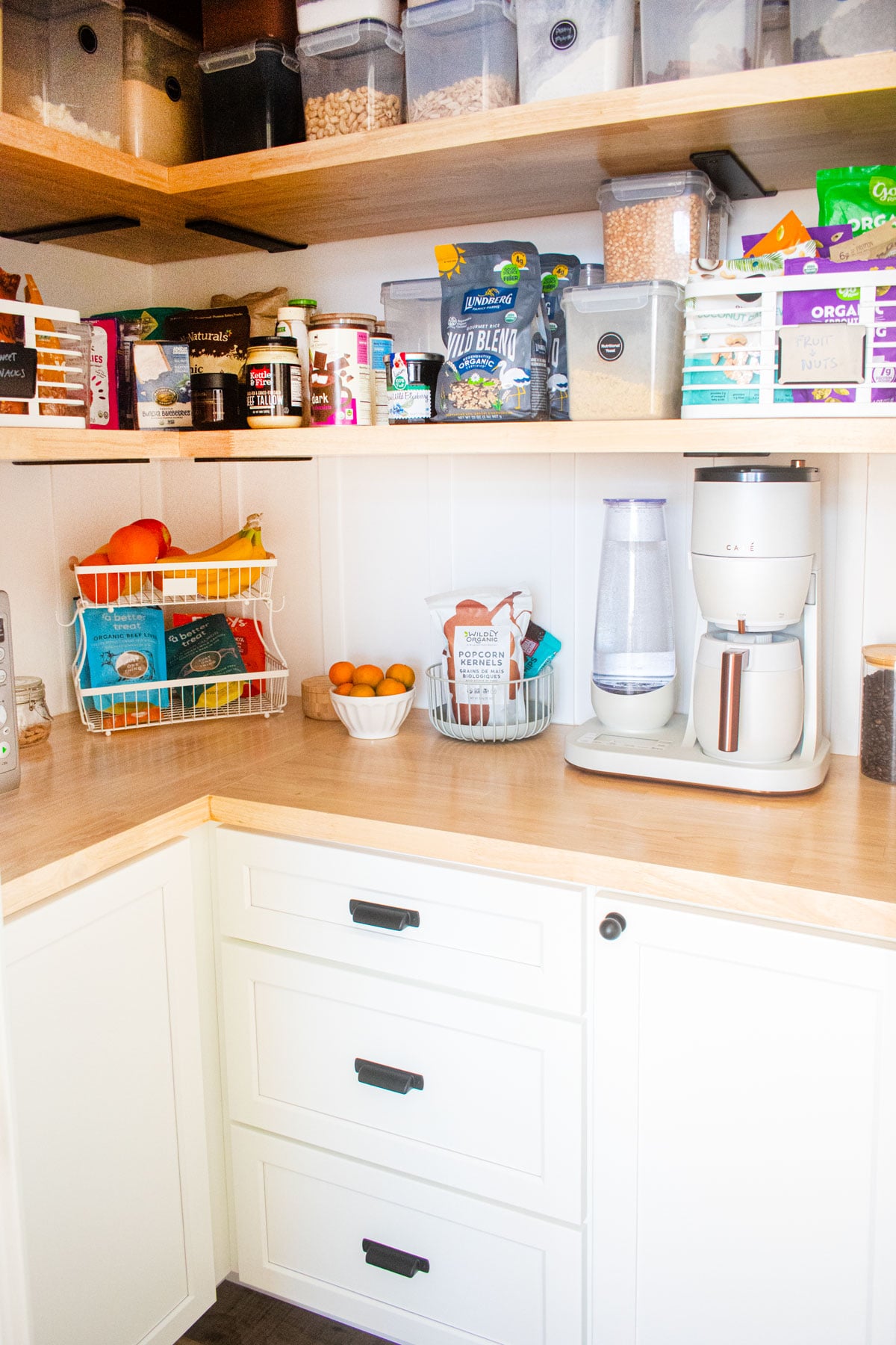 diy kitchen corner pantry with white cabinets and wood counters and wood shelving with pantry storage bins.