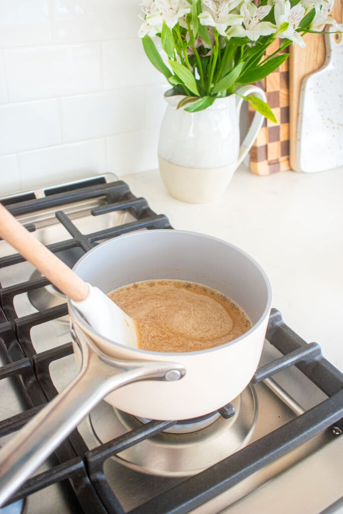wet ingredients for peanut butter honey granola in a small pot being stirred on top of a stovetop.