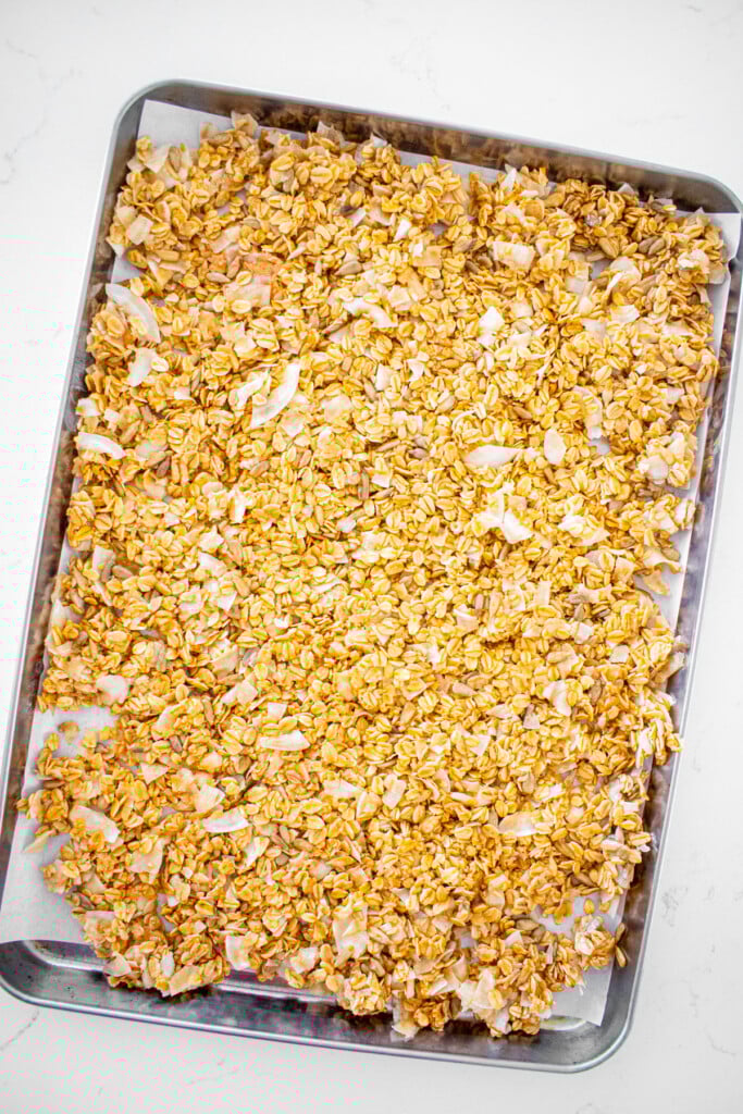 peanut butter honey granola for dogs spread out on a baking sheet on a white marble counter.