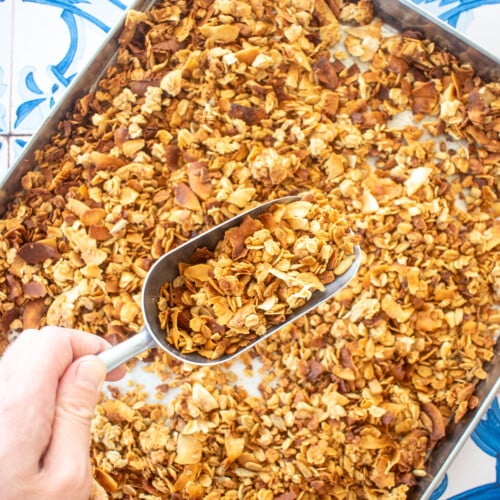 peanut butter honey granola for dogs on a baking sheet on a blue tile table, woman scooping it with a scoop.