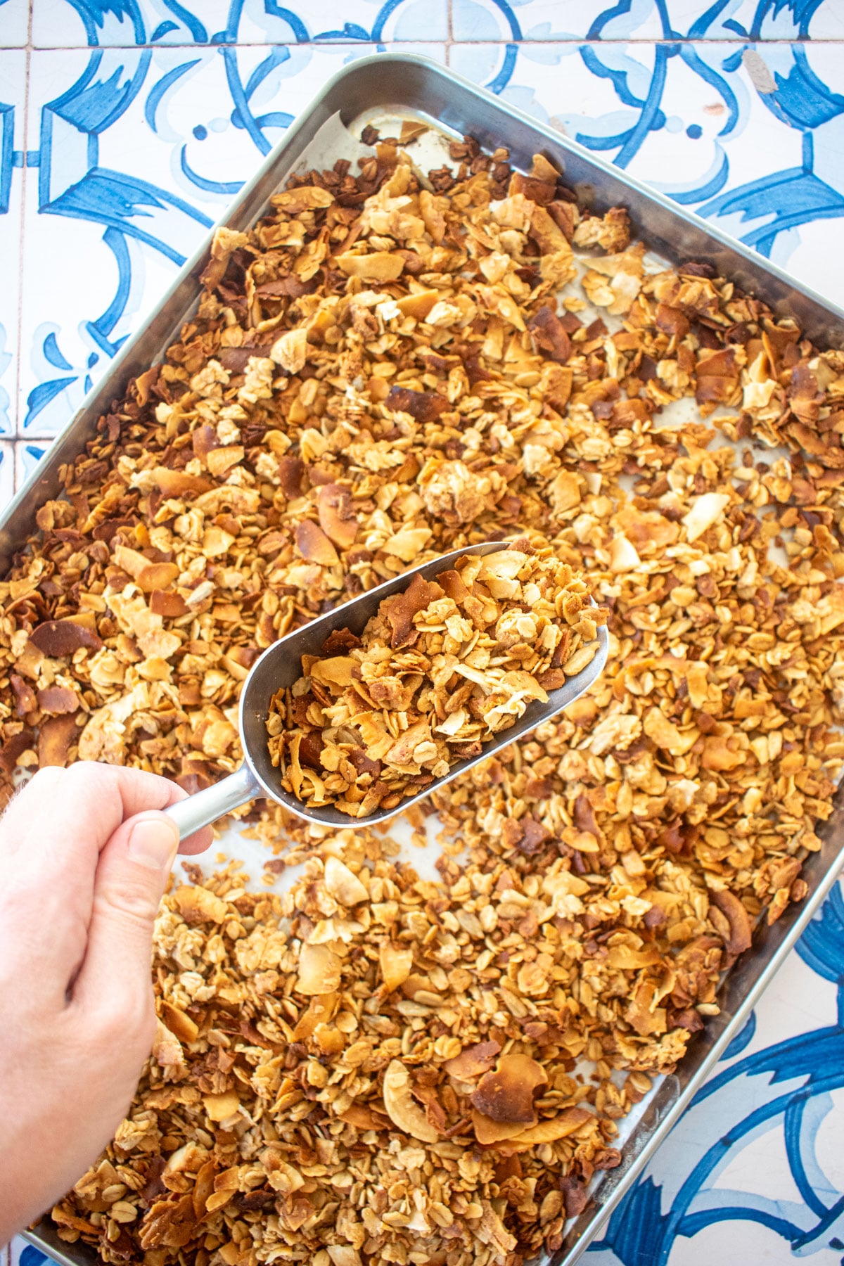 peanut butter honey granola for dogs on a baking sheet on a blue tile table, woman scooping it with a scoop.