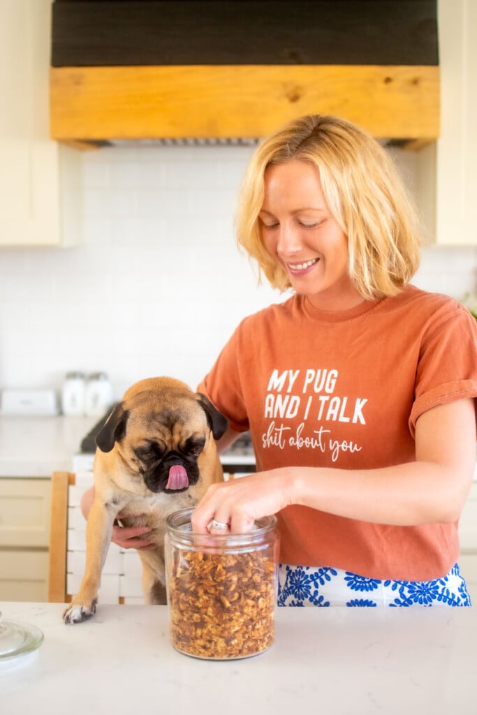 woman and pug in the kitchen eating granola out of a glass jar.