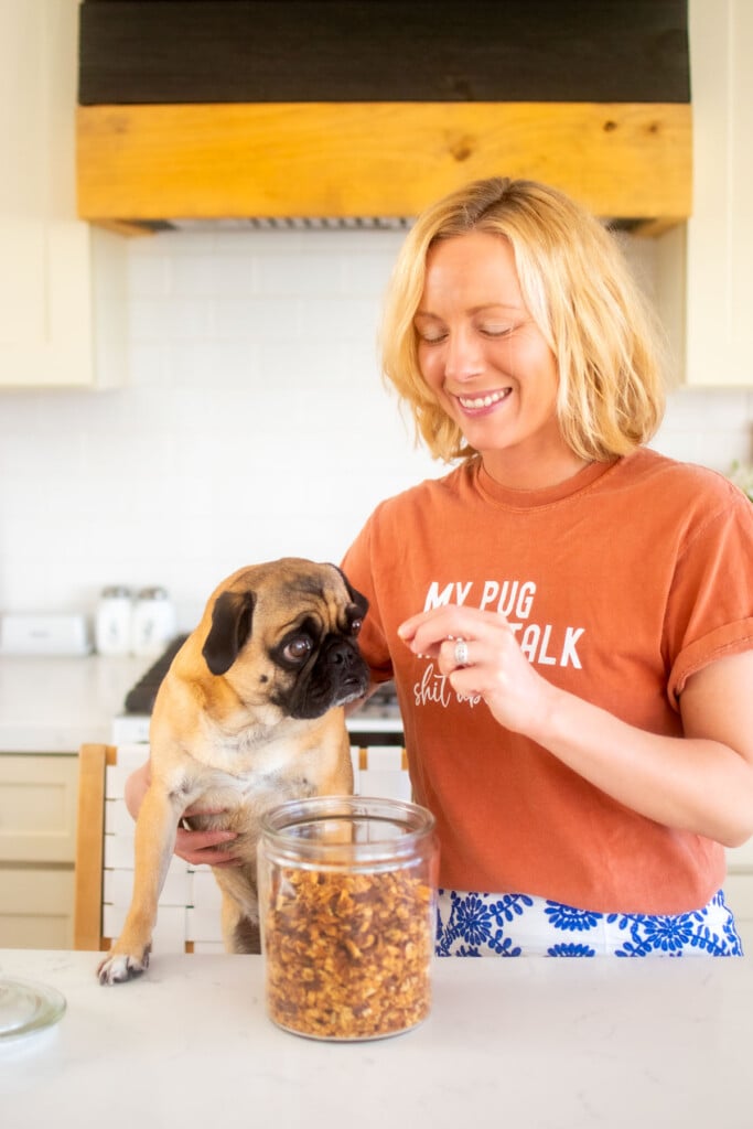 woman and pug in the kitchen eating granola out of a glass jar.