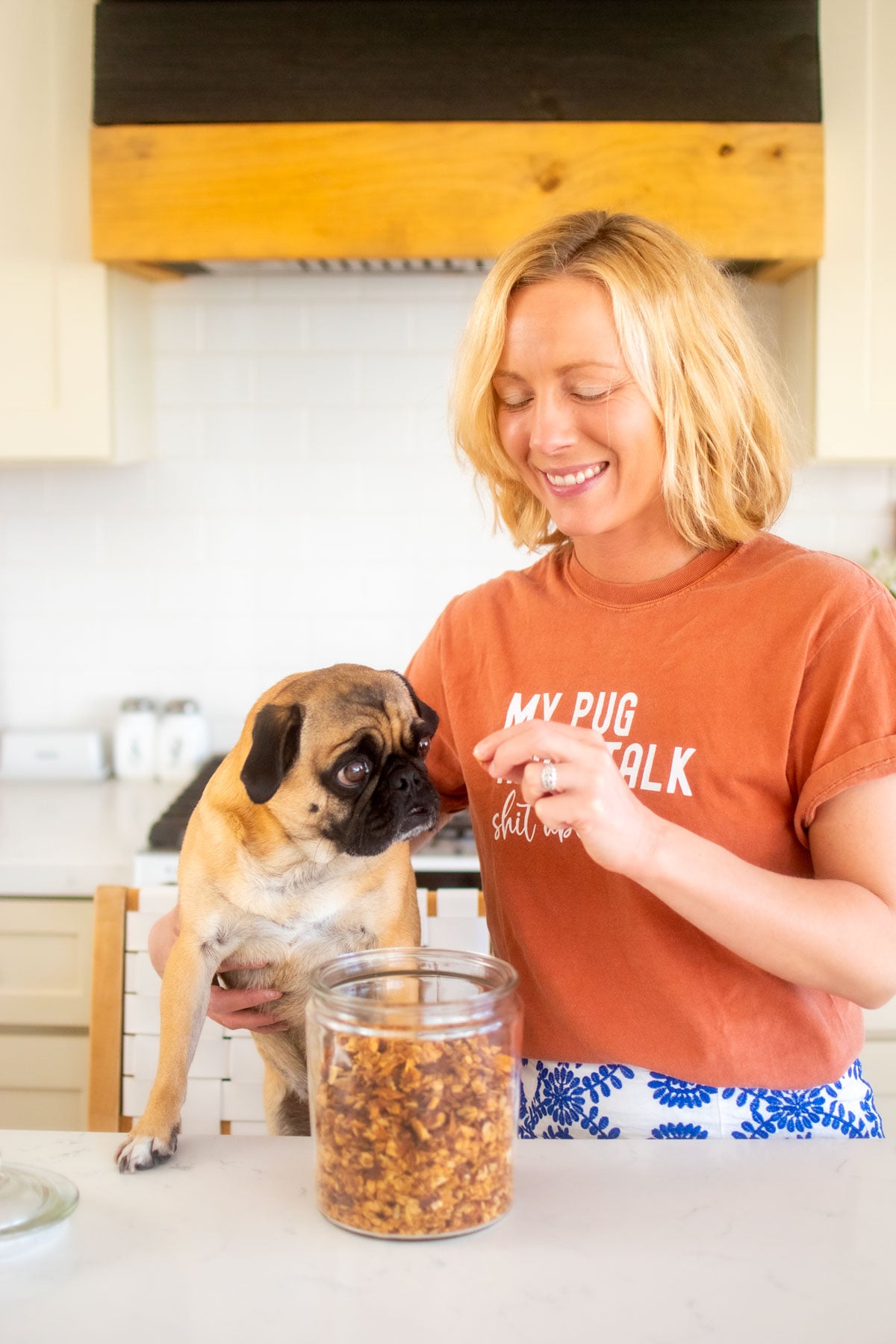 woman and pug in the kitchen eating granola out of a glass jar.