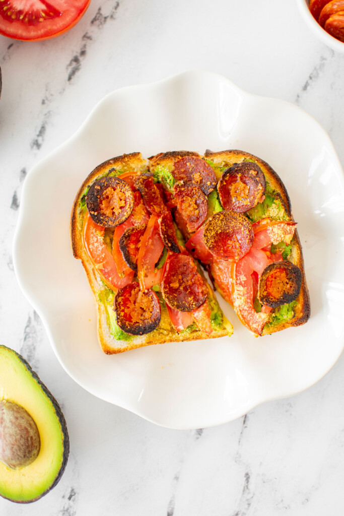 pizza avocado toast cut in half on a white plate on a marble countertop.