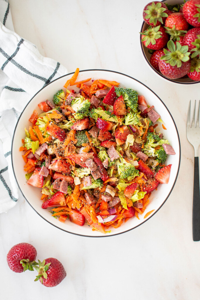 strawberry balsamic broccoli salad in a white bowl on a marble countertop with fresh strawberries in a bowl.