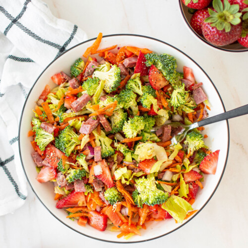 strawberry balsamic broccoli salad in a white bowl on a marble countertop with a fork in it.