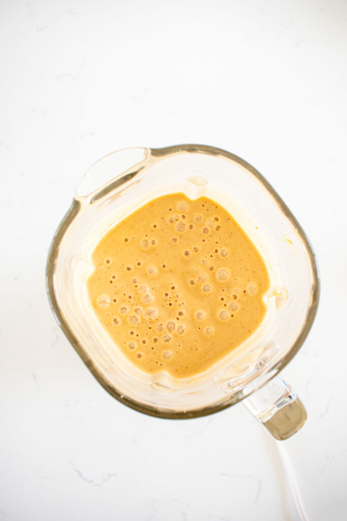 glass blender with peanut butter ice cream mixture in it on a white countertop.