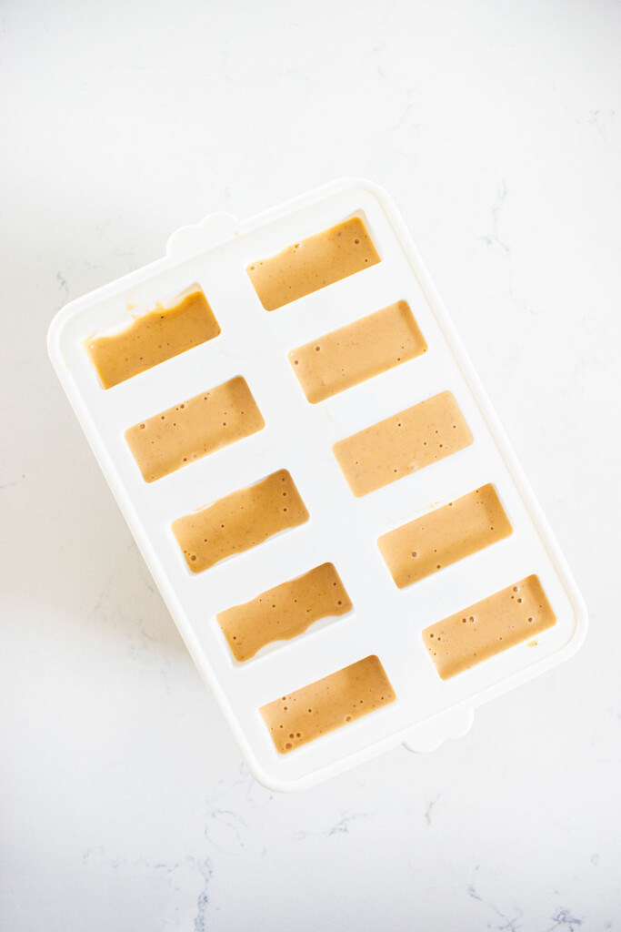 peanut butter ice cream in a silicone popsicle mold on a white countertop.