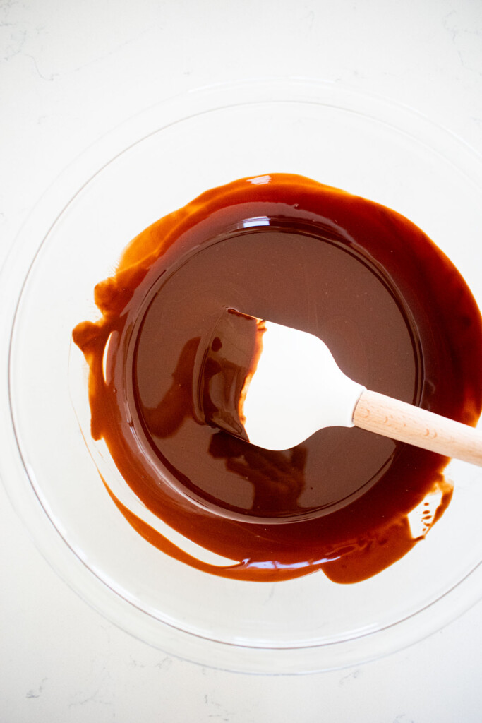 melted dark chocolate in a glass mixing bowl on a white counter.