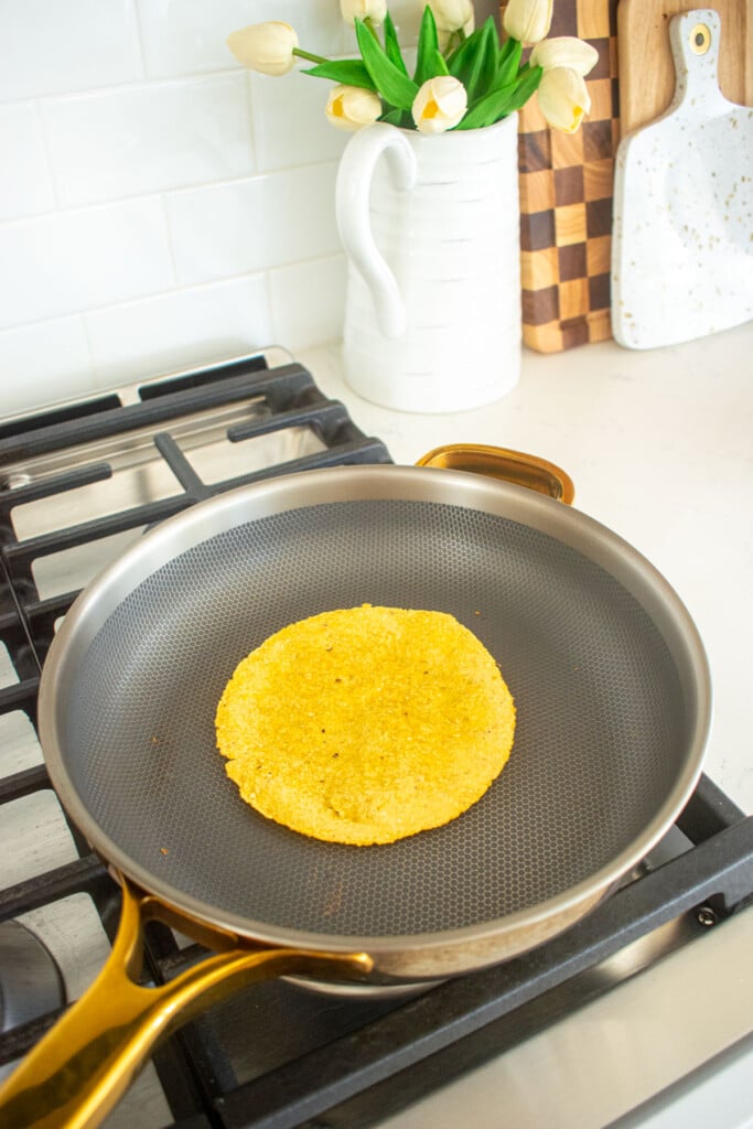 corn tortilla being warmed in a skillet on the stovetop.