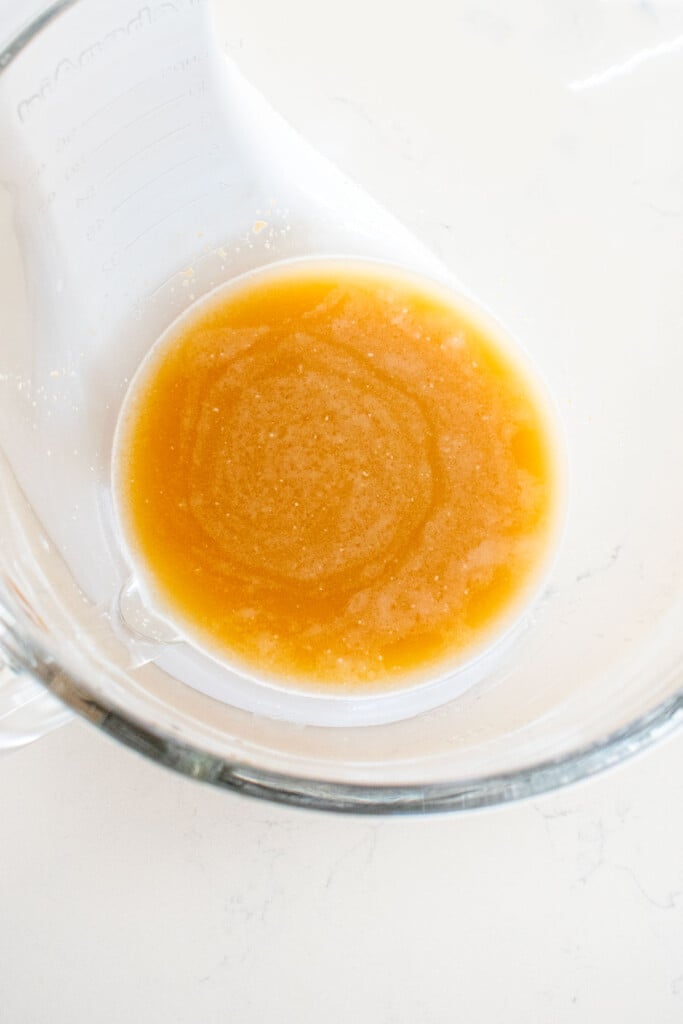 instant yeast, water and bone broth in a glass mixing bowl on a white marble countertop.