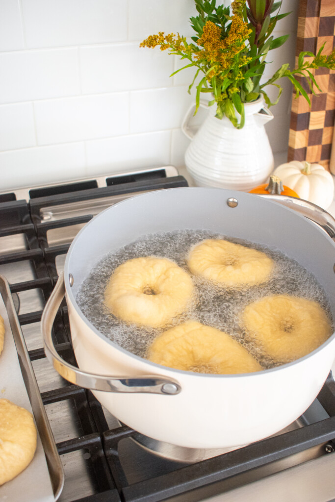 bagels being boiled in poaching liquid in a large pot on the stovetop.