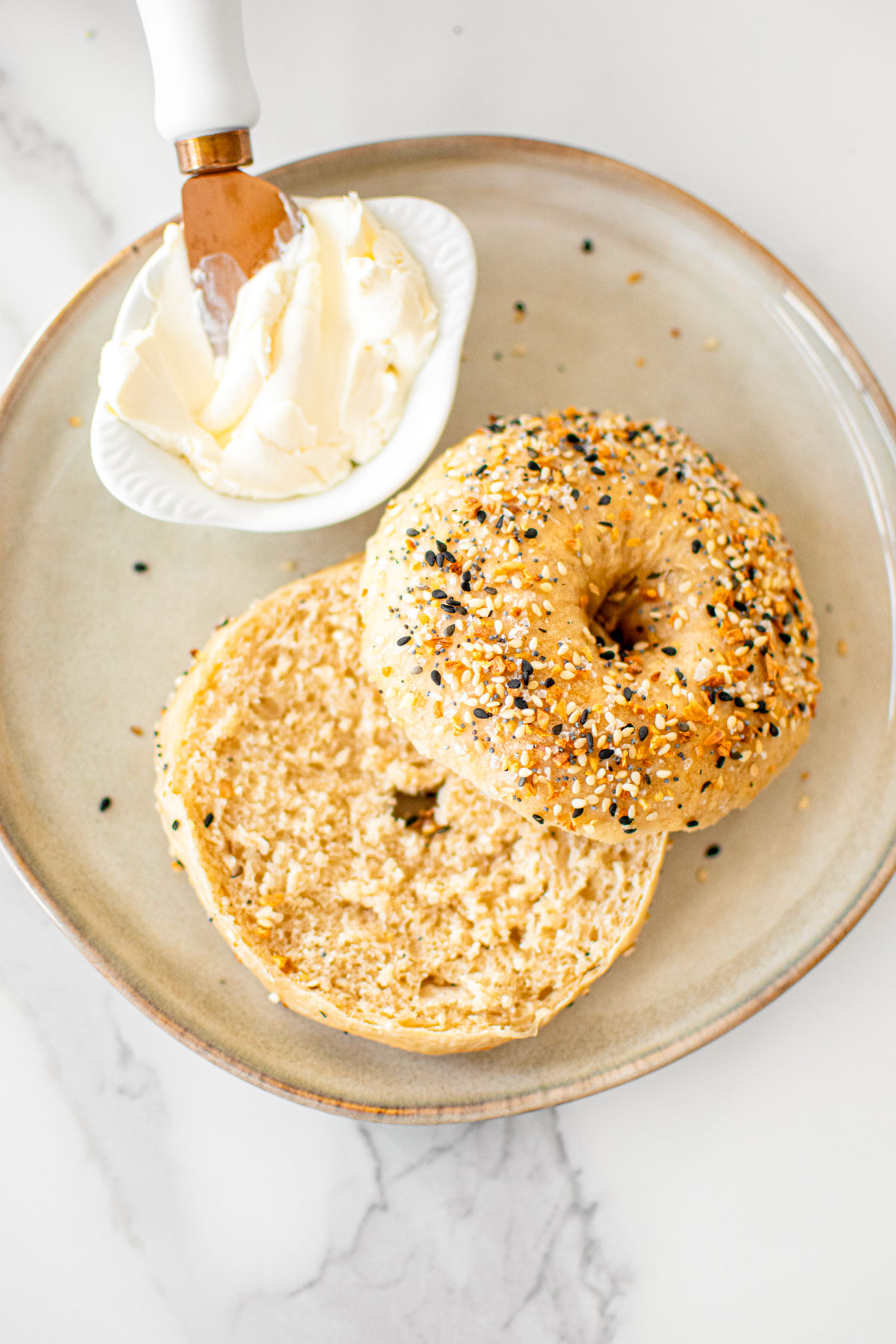 bone broth everything bagel cut in half with a small bowl of cream cheese on a plate.