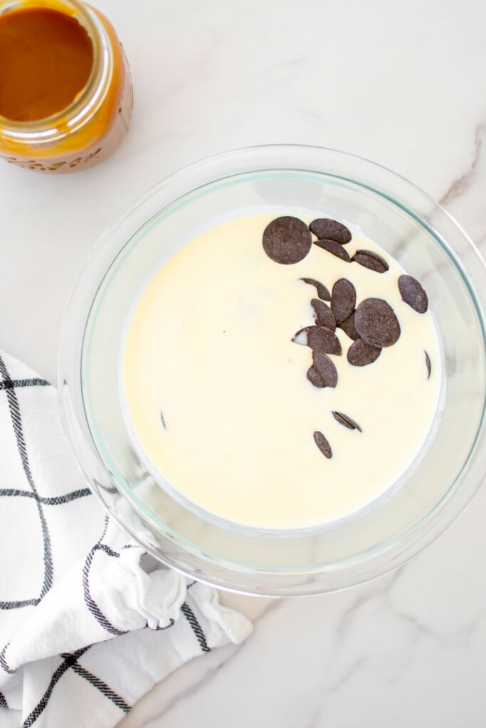 dark chocolate and heavy whipping cream in a glass mixing bowl on a white marble counter.