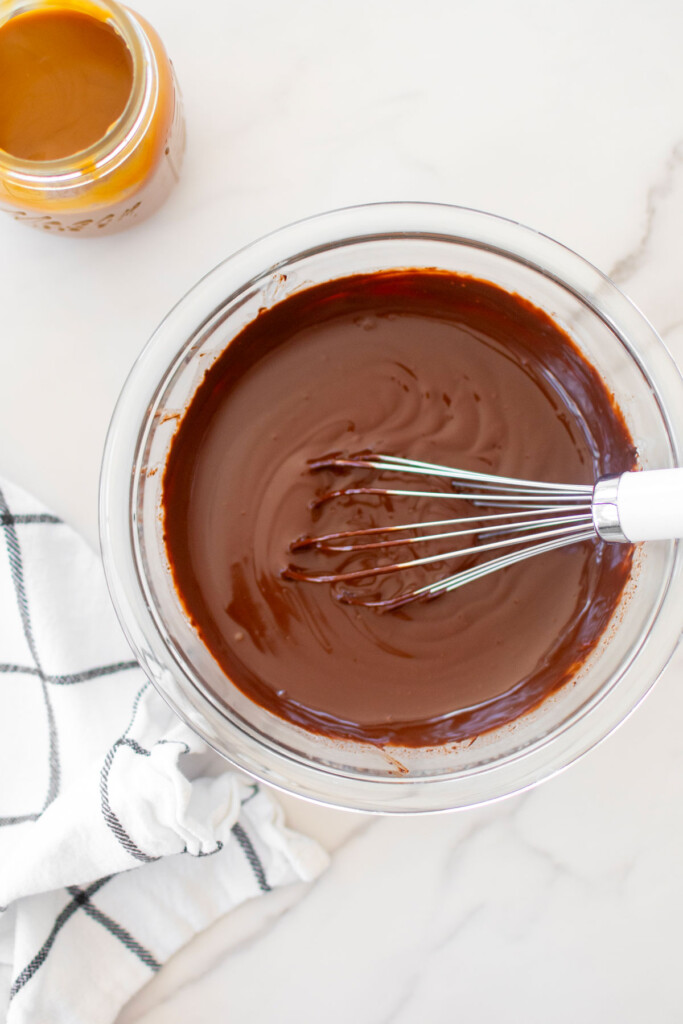 chocolate peanut butter caramel ganache frosting being whisked together in a glass mixing bowl.