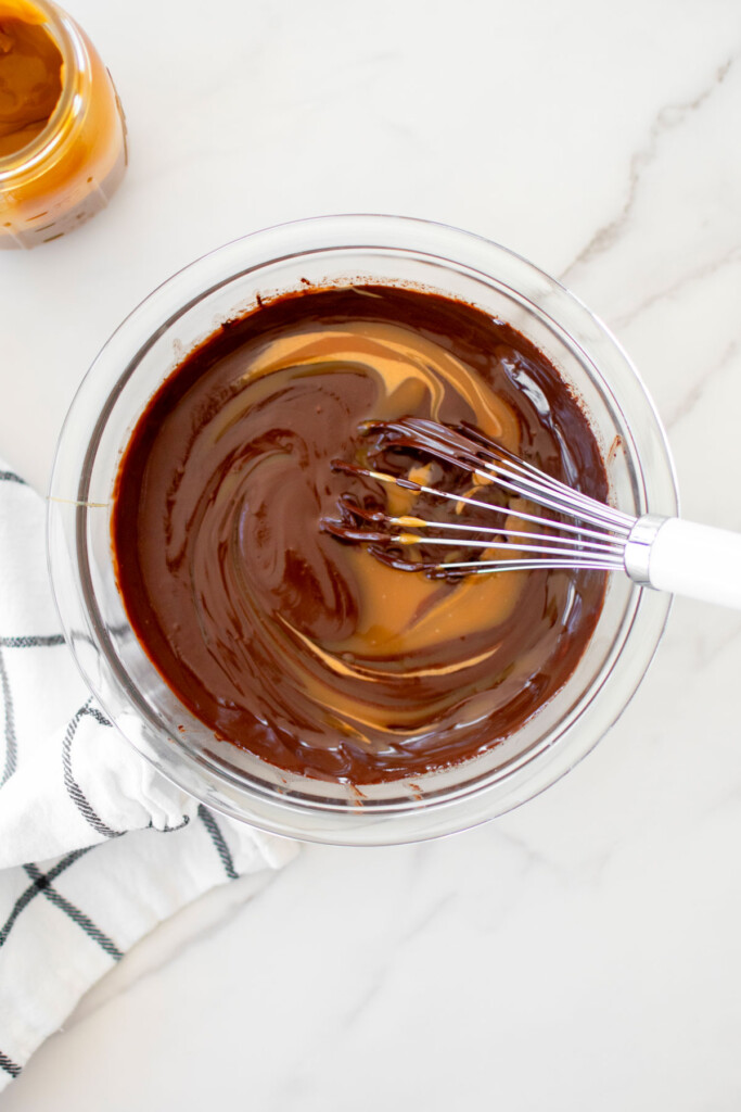 chocolate peanut butter caramel ganache frosting being whisked together in a glass mixing bowl.