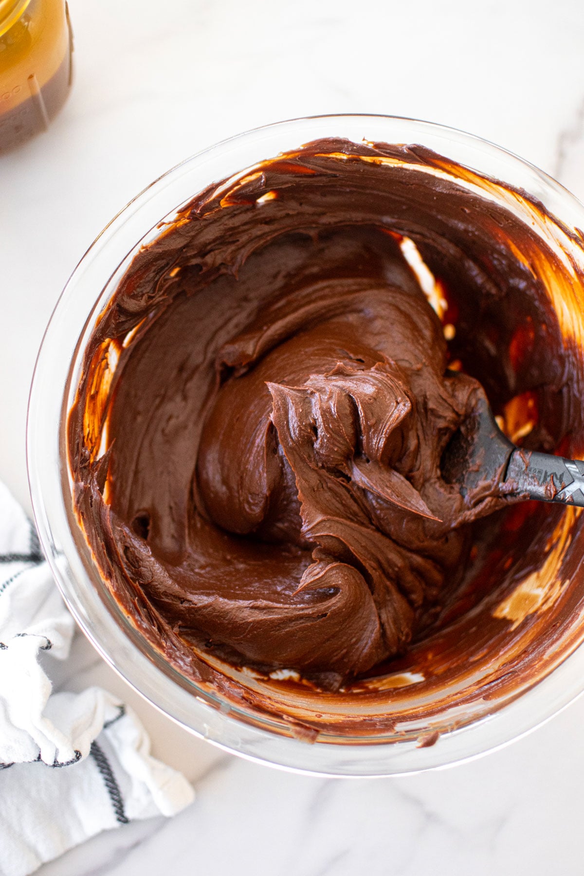 chocolate peanut butter caramel ganache frosting in a glass mixing bowl with a spatula on a white marble counter.
