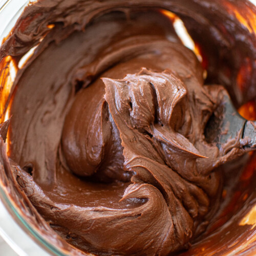 chocolate peanut butter caramel ganache frosting in a glass mixing bowl with a spatula on a white marble counter.