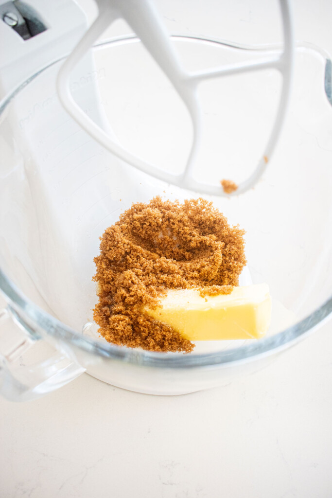 butter and sugar in a glass mixing bowl on a white marble counter.
