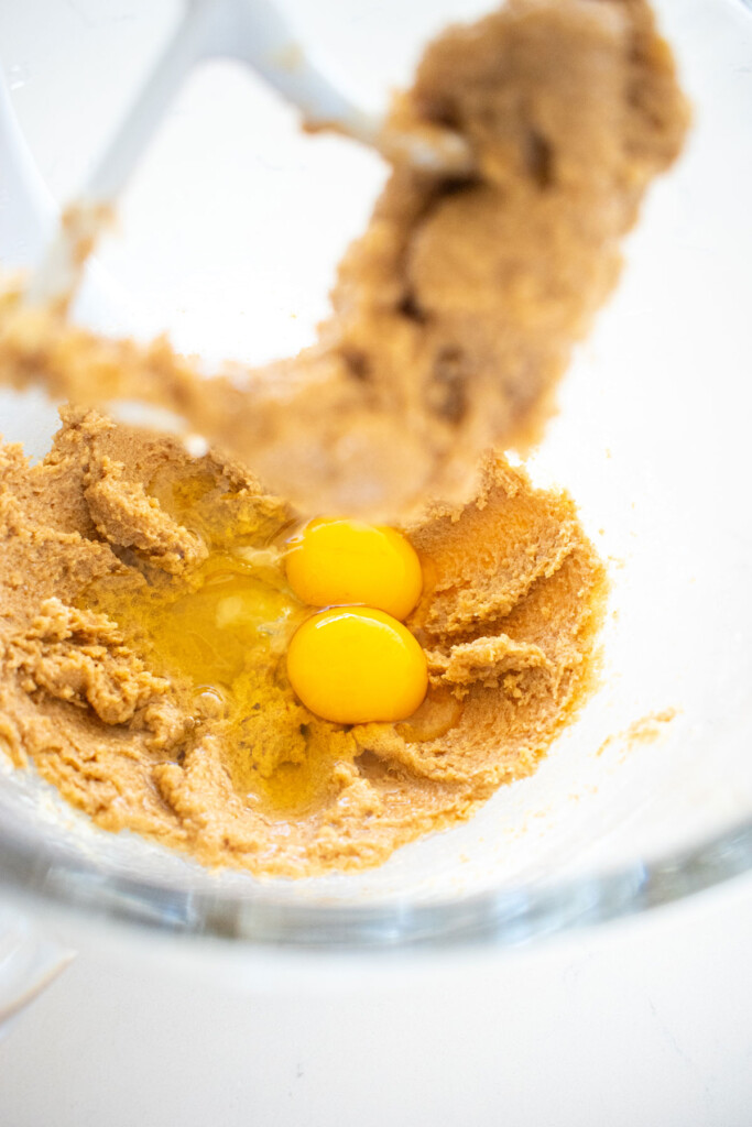 creamed butter and sugar with eggs in a glass mixing bowl on a white marble counter.