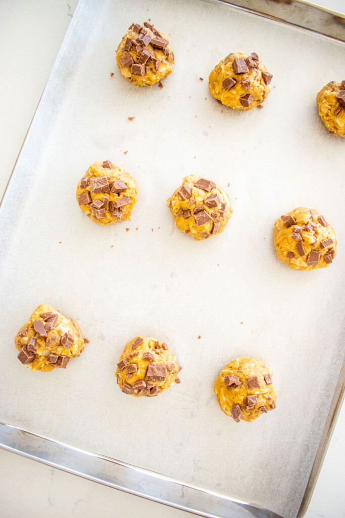 coconut milk chocolate chunk cookie dough balls on a baking sheet on a marble counter.