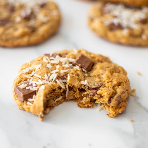 coconut milk chocolate chunk cookie with a bite taken out on a marble counter.