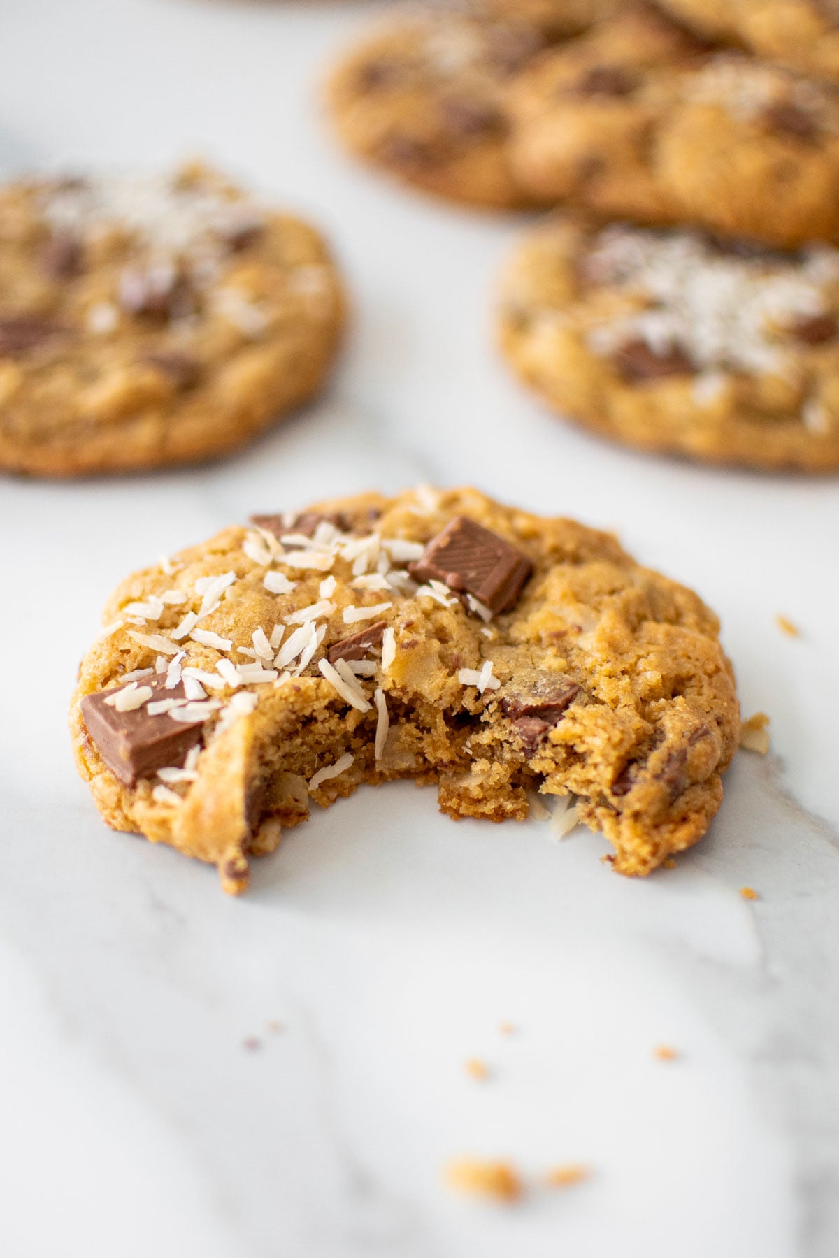 coconut milk chocolate chunk cookie with a bite taken out on a marble counter.