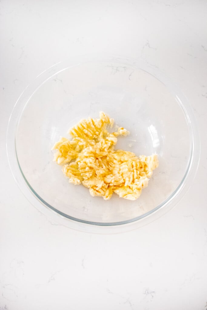 mashed up banana in a glass mixing bowl on a white marble counter.