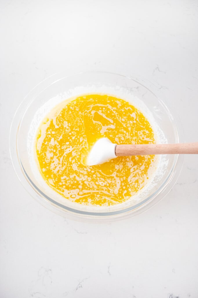 wet ingredients for eggless apple cinnamon waffles in a glass mixing bowl on a white marble counter.