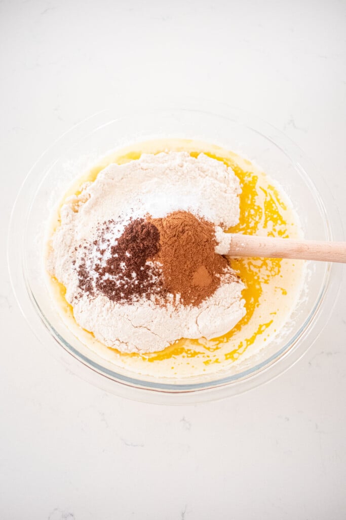 ingredients for eggless apple cinnamon waffles in a glass mixing bowl on a white marble counter.