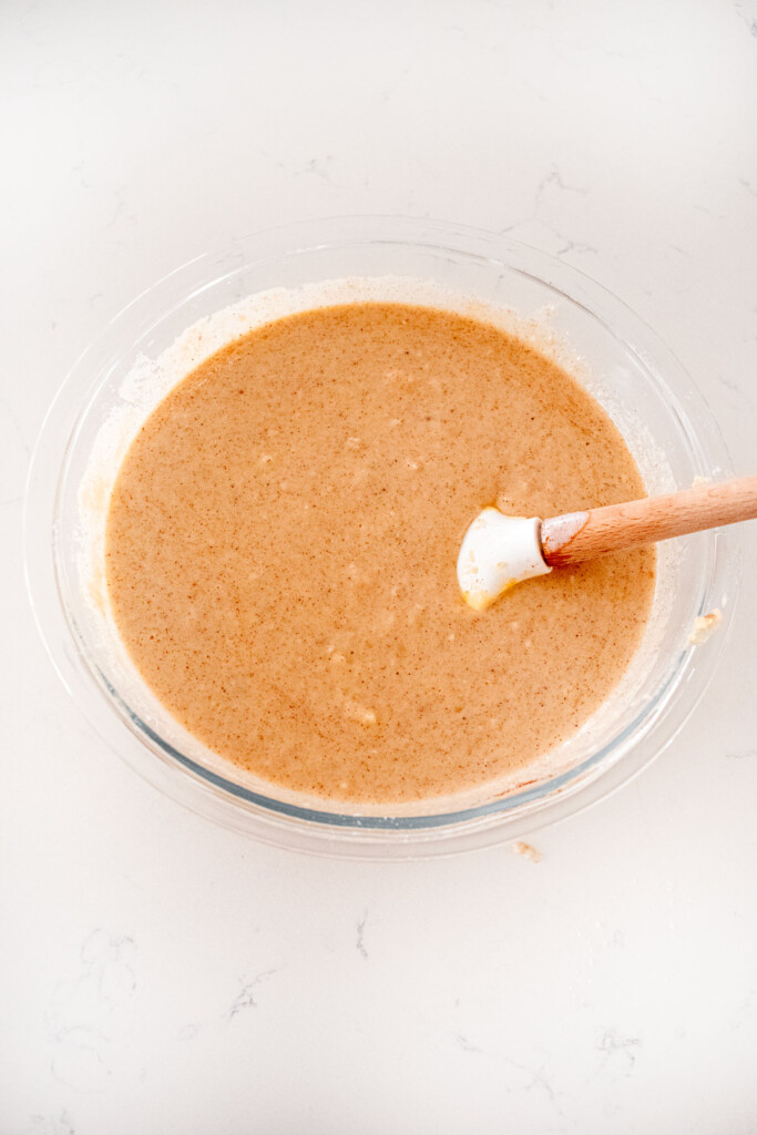 eggless apple cinnamon waffle batter in a glass mixing bowl on a white marble counter.