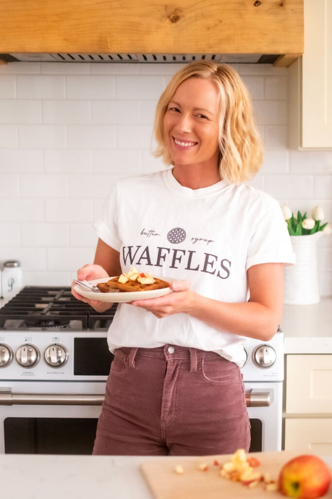 woman holding a plate of eggless apple cinnamon waffles in the kitchen.