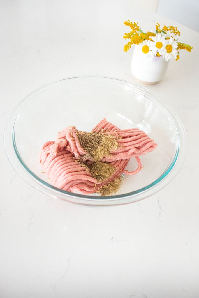 glass bowl with ground turkey and spices on a marble counter with a small vase of fresh flowers.